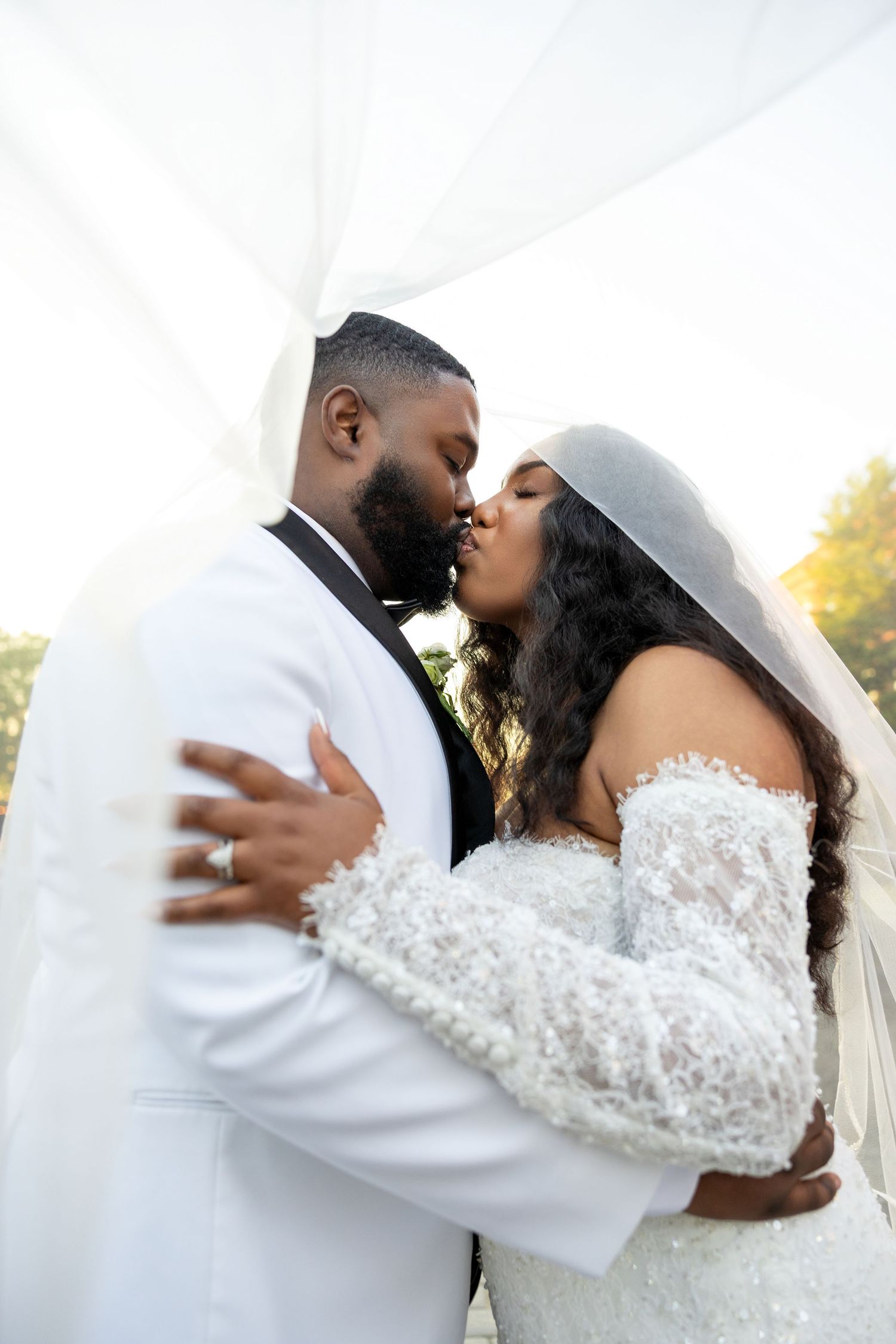 A bride and groom share a first kiss under white draped fabric during their outdoor wedding ceremony.