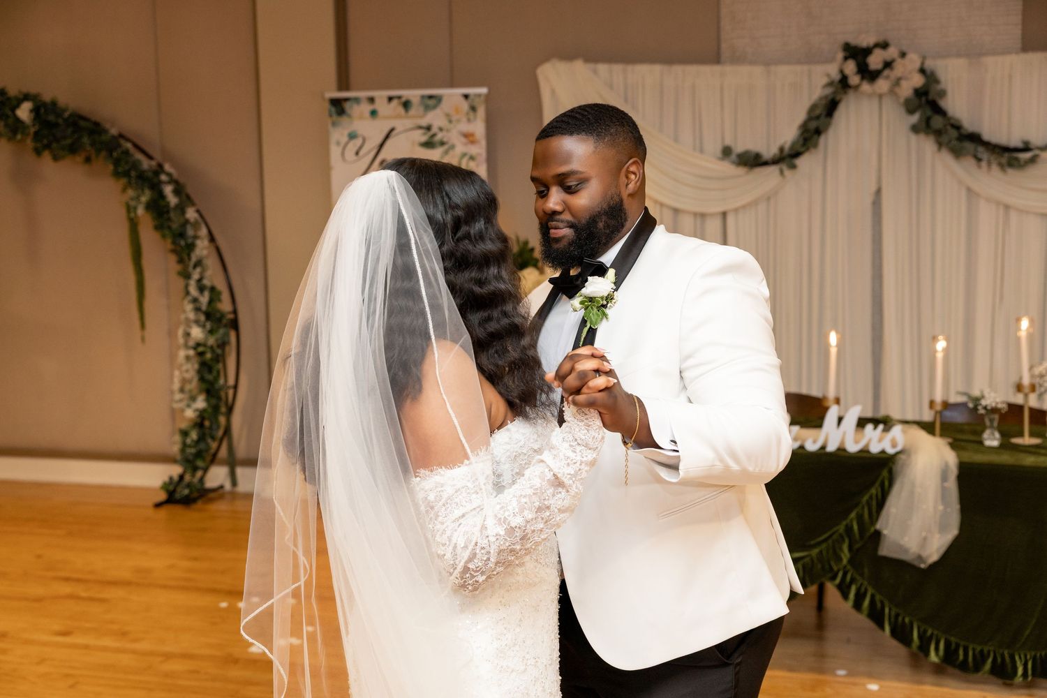 Bride and groom share first dance at elegant wedding reception with floral arch backdrop.