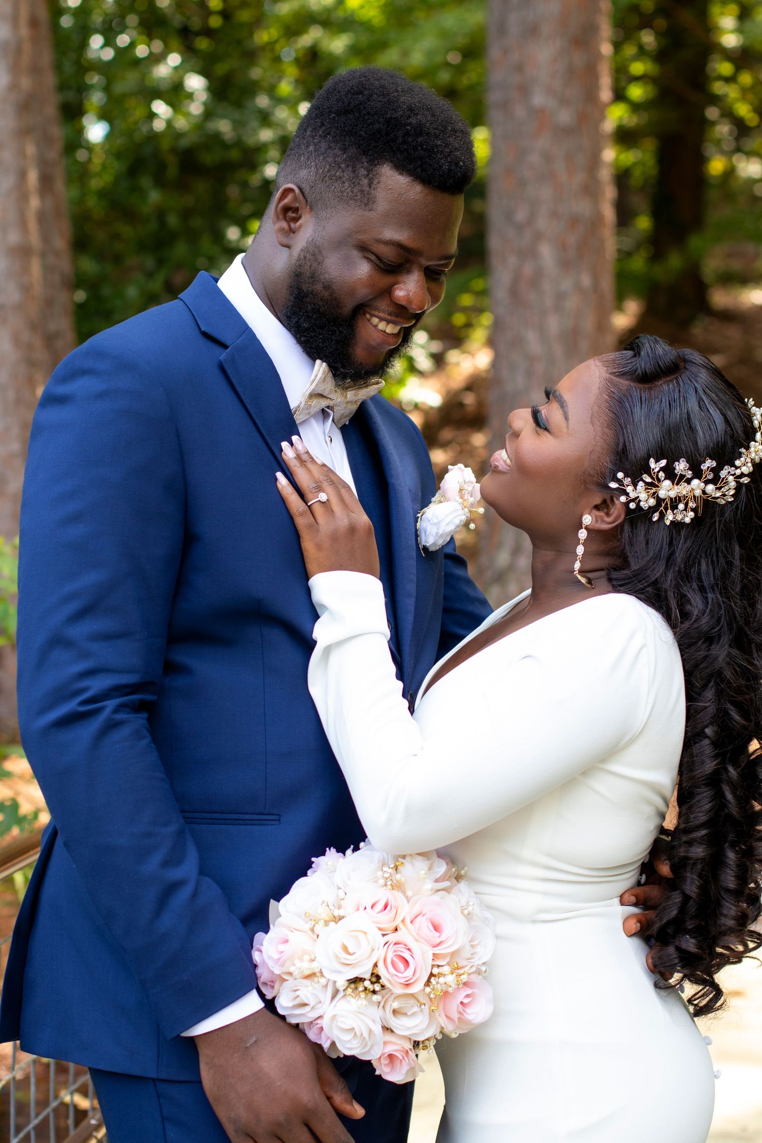 A loving couple in wedding attire share an intimate moment outdoors, with the bride holding a pink rose bouquet.