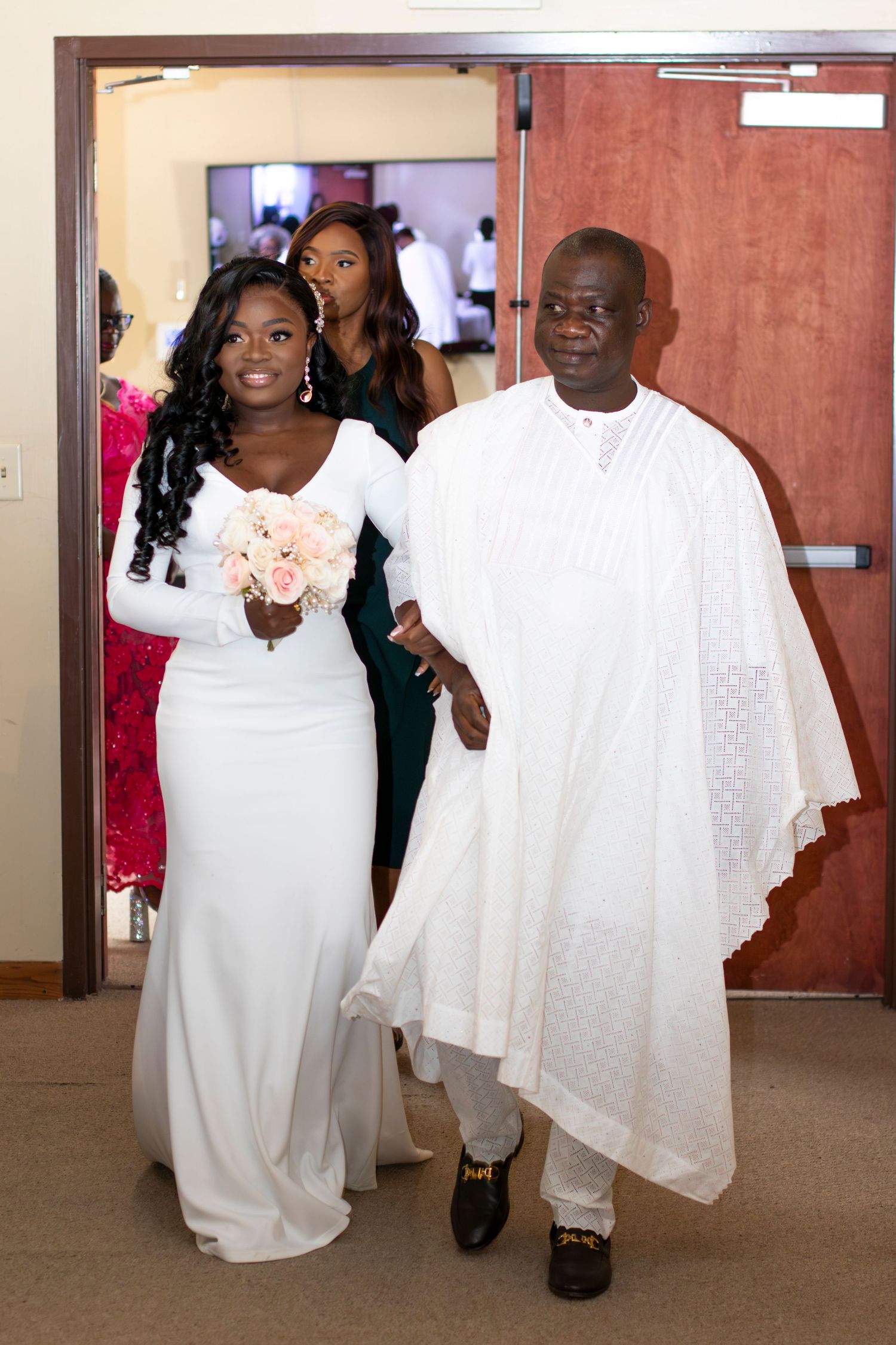A bride in a white long-sleeve gown walks arm in arm with someone wearing traditional white agbada at a wedding ceremony.