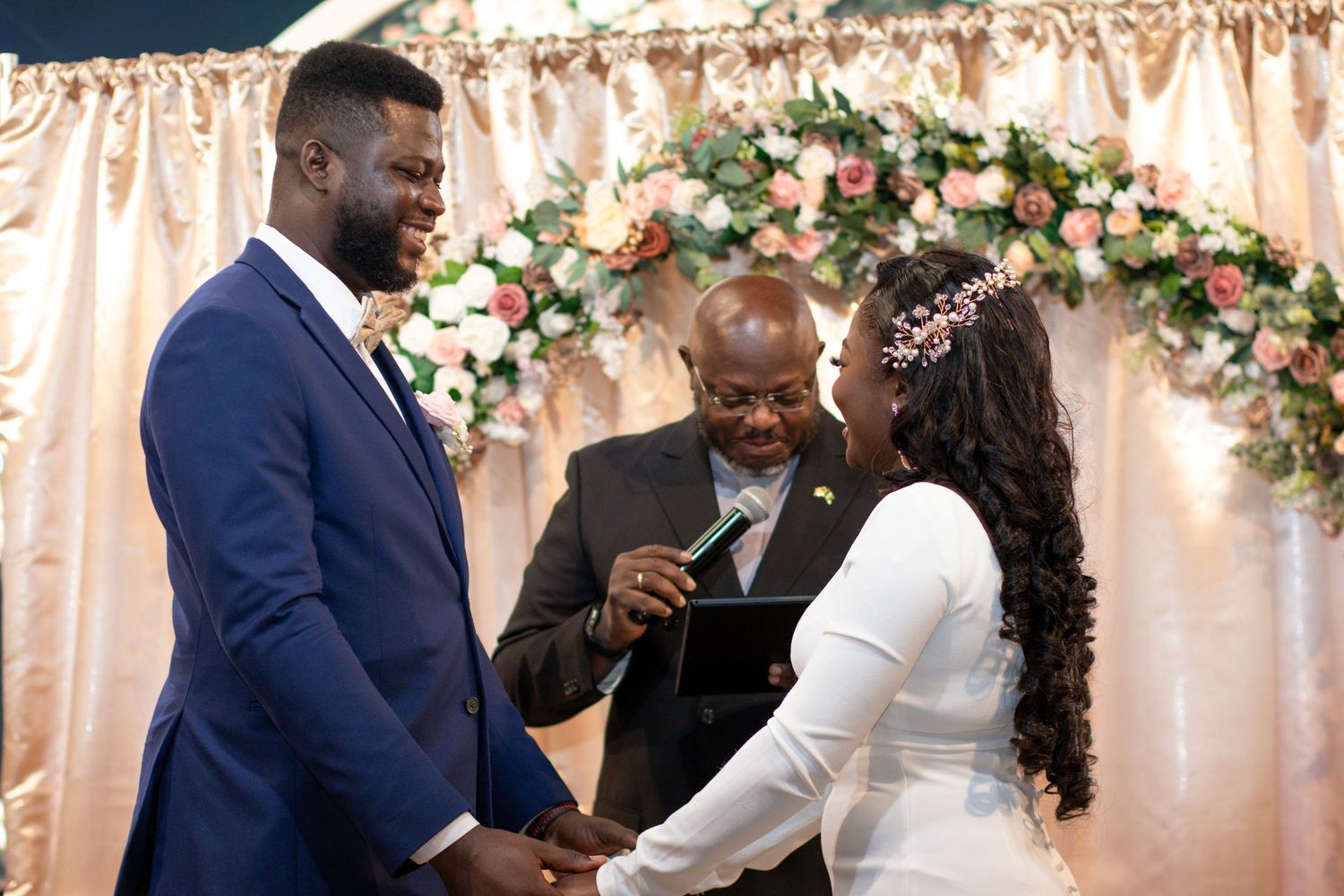 Wedding ceremony takes place under a floral arch with couple exchanging vows in front of an officiant.