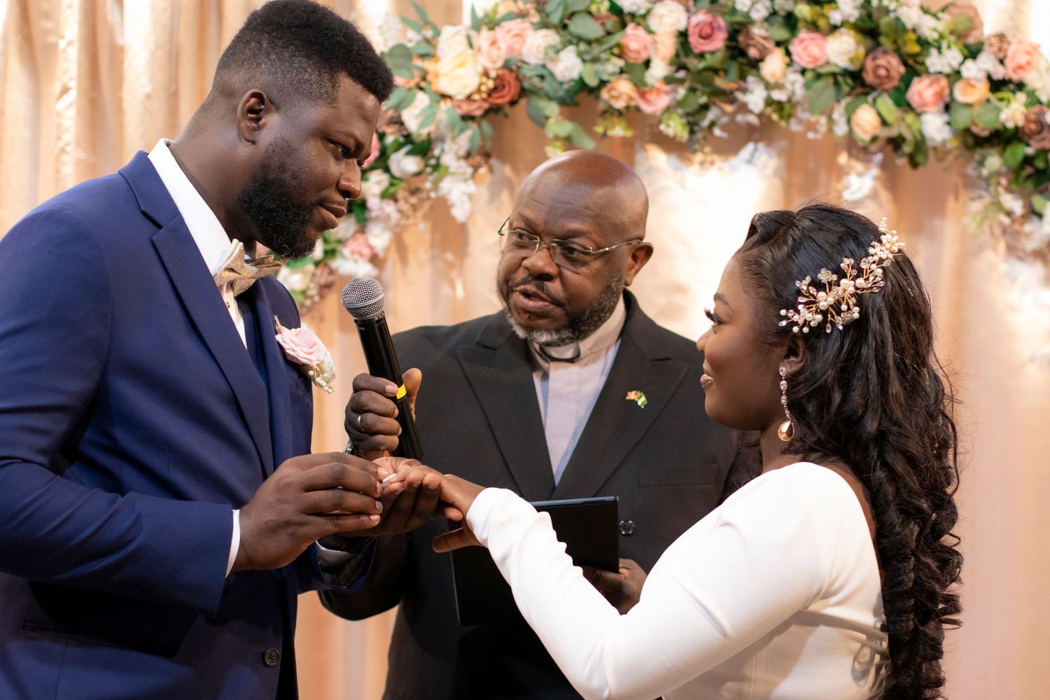 A beautiful wedding ceremony takes place in front of a floral arch with pink and peach roses.