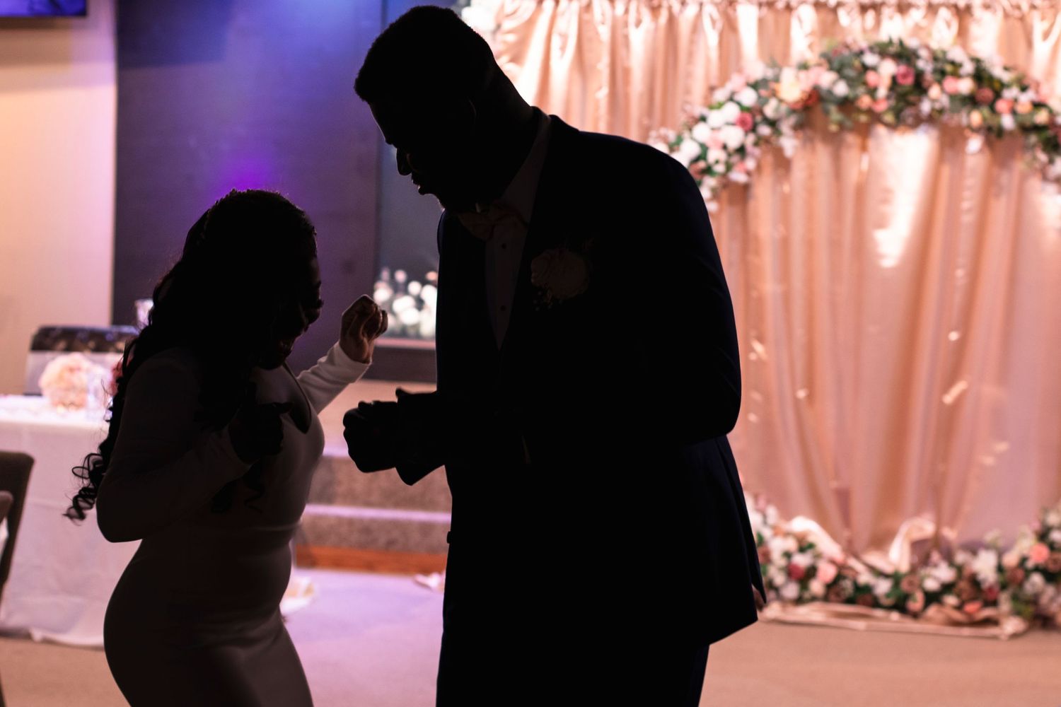 Silhouettes of two figures dancing together at an event with pink decorative backdrop and lighting.