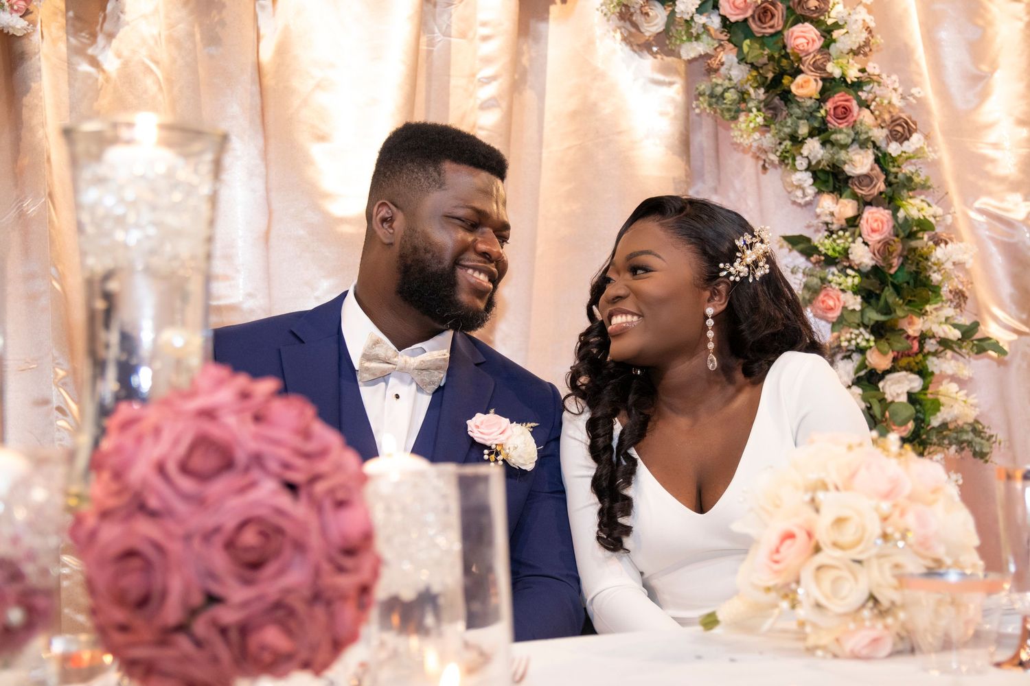 Newlyweds share a joyful moment at their wedding reception with pink floral decorations and elegant decor.
