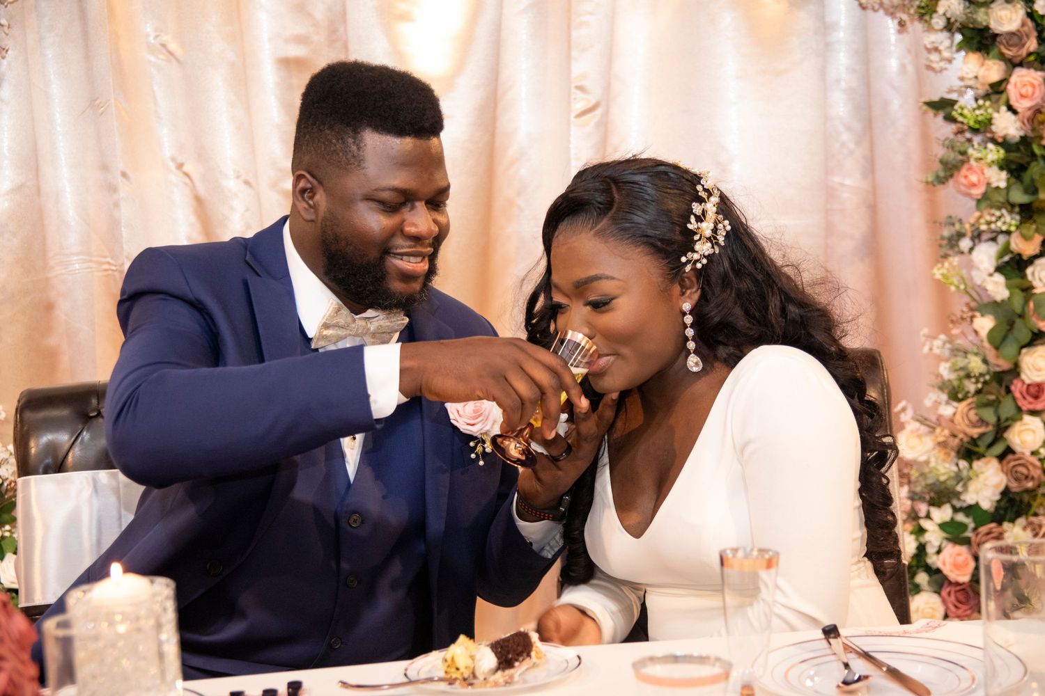 A happy couple shares a sweet moment at their wedding reception while seated at a decorated table with floral decor.