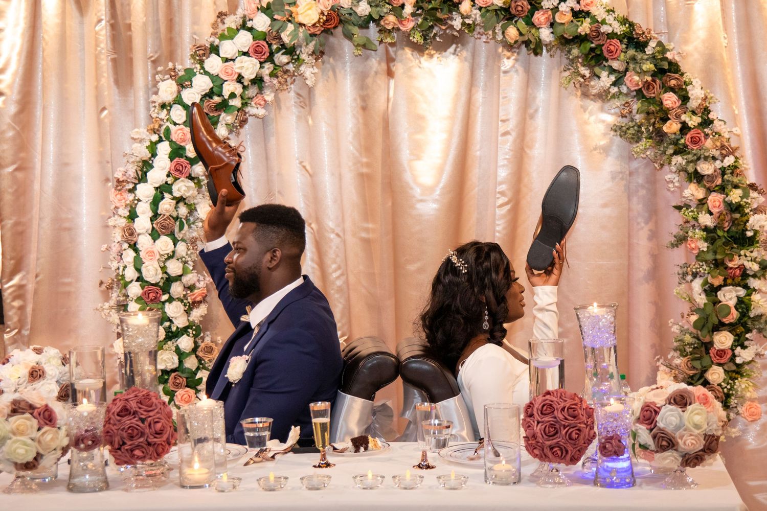 A decorated wedding reception table with a floral arch and pink decor as a couple celebrates at their sweetheart table.