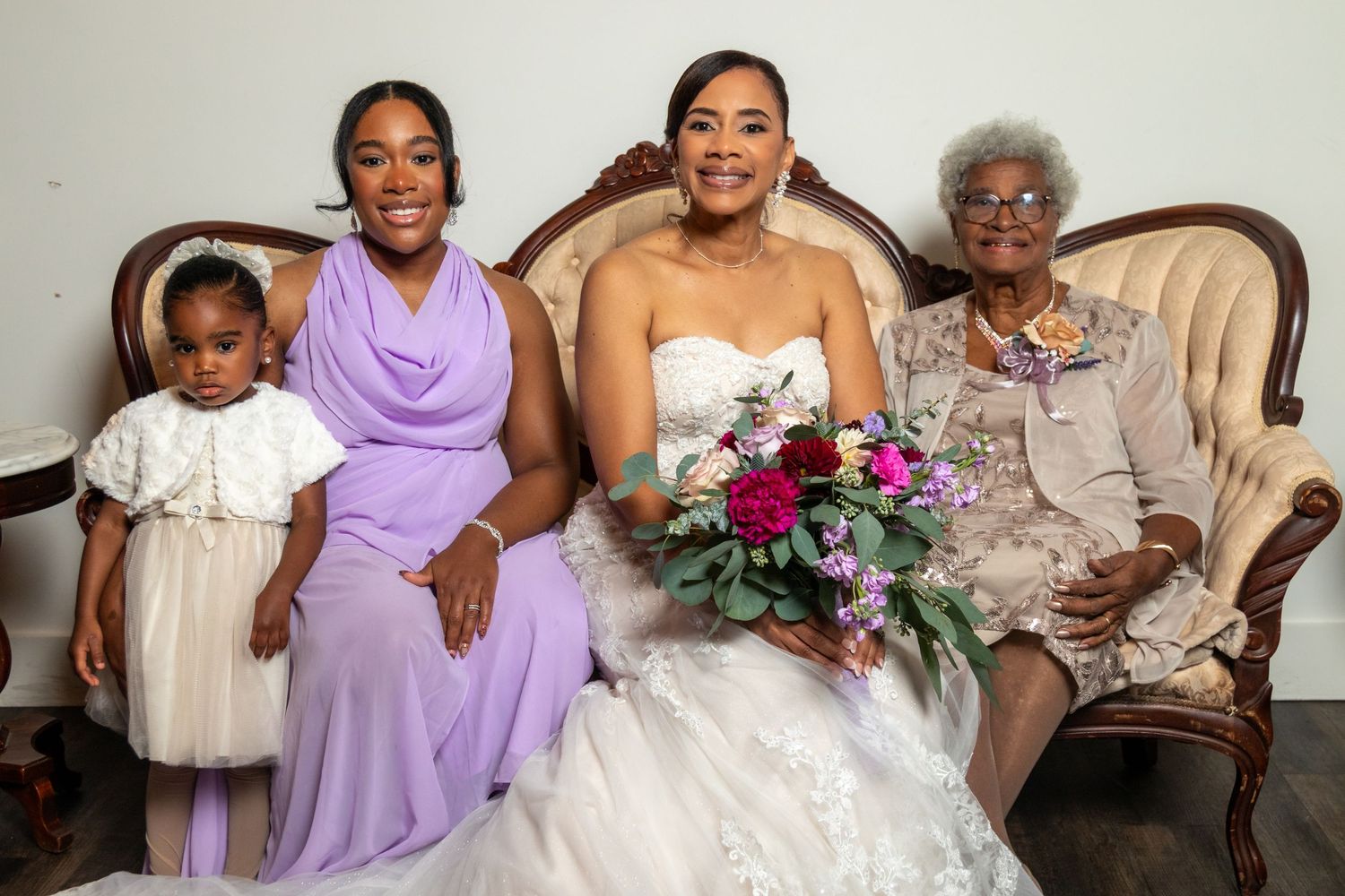 A multigenerational wedding portrait featuring a bride sitting with family members on an elegant sofa.