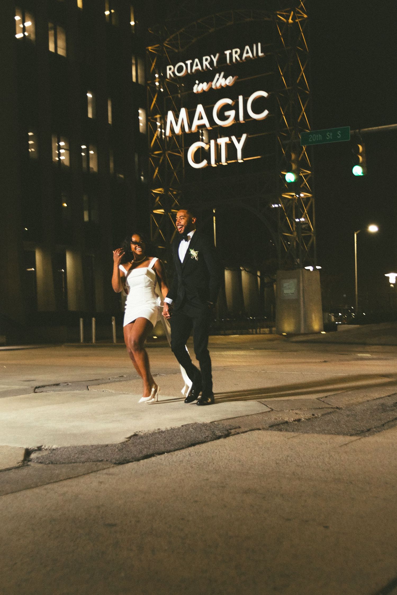 A couple dances together at night under an illuminated 'Rotary Trail in the Magic City' sign.