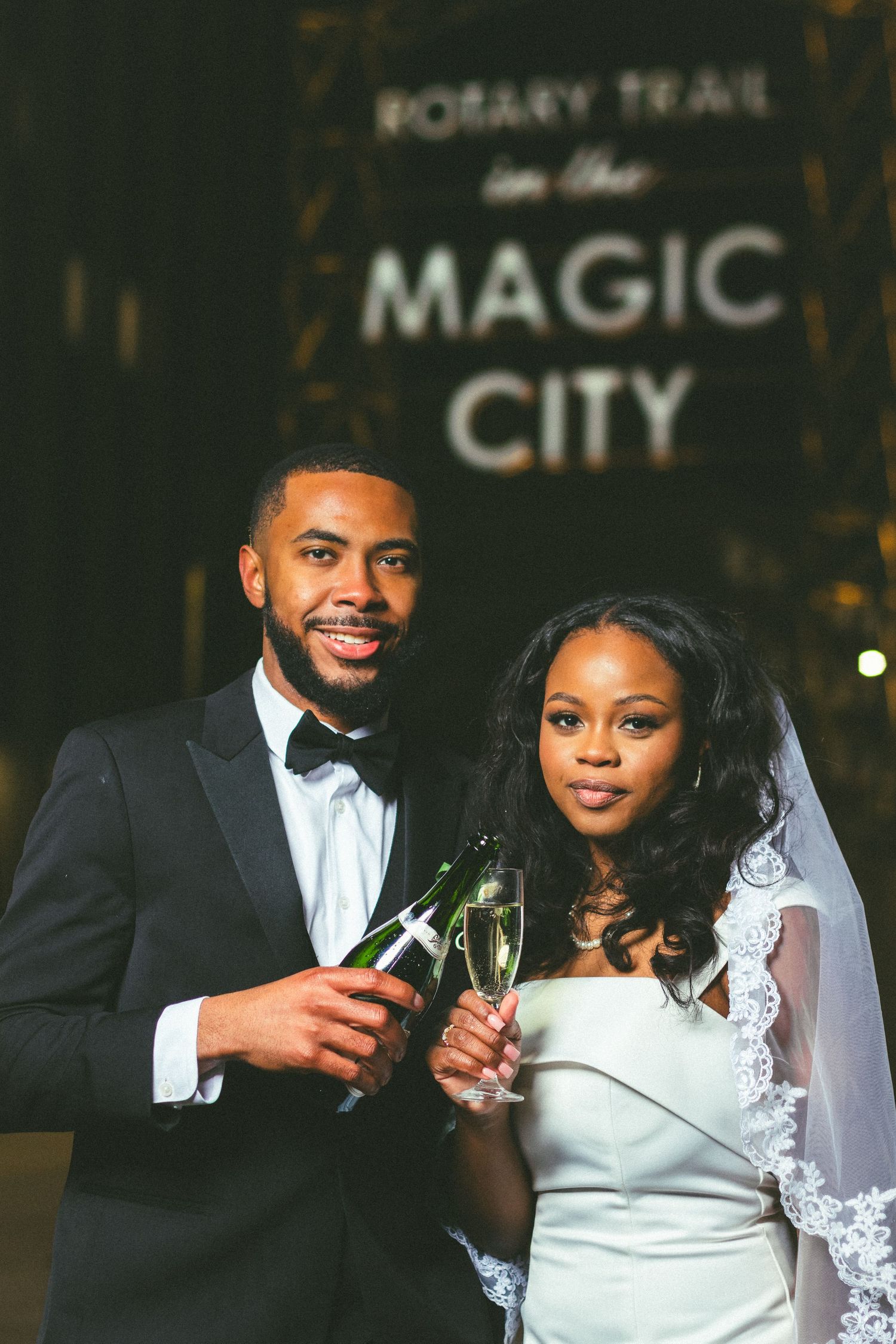 A couple toasts with champagne beneath the illuminated Magic City Rotary Trail sign.