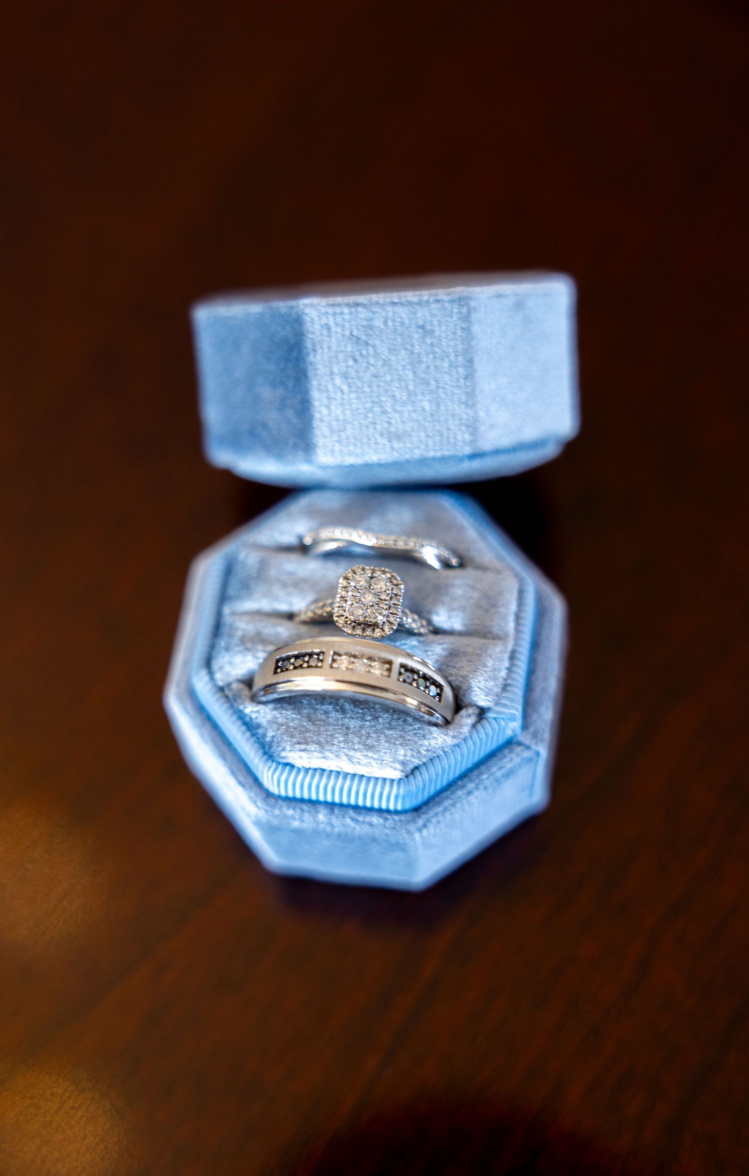 Wedding rings nestled in a light blue velvet ring box on a dark wooden surface.