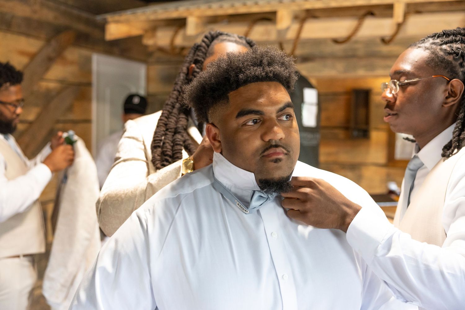 Wedding preparation scene showing groom preparation with bow tie adjustments.