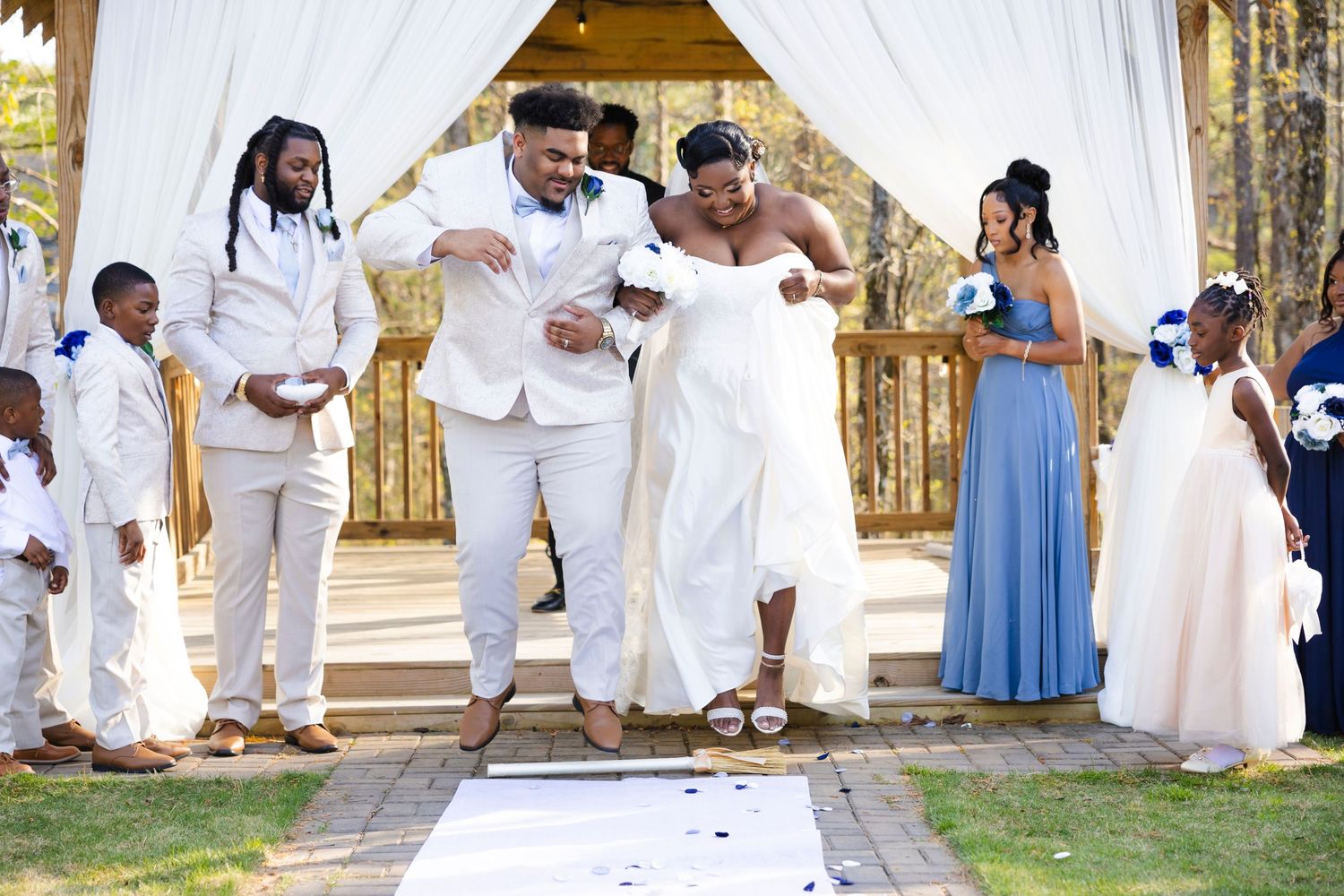 Wedding party celebrating with a traditional jumping of the broom ceremony at an outdoor venue.