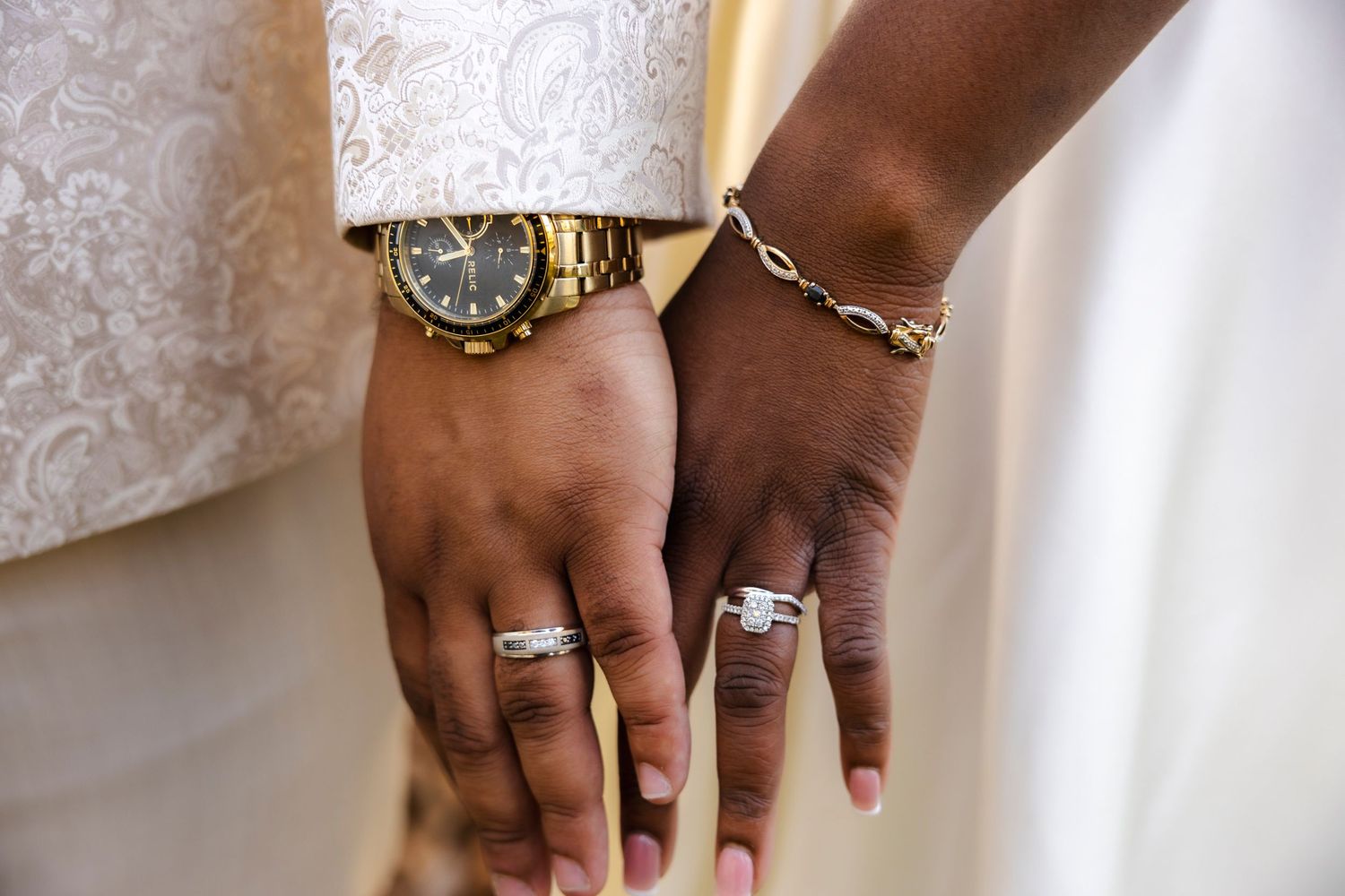 Close-up of two hands with wedding rings, watch, and bracelet accessories.