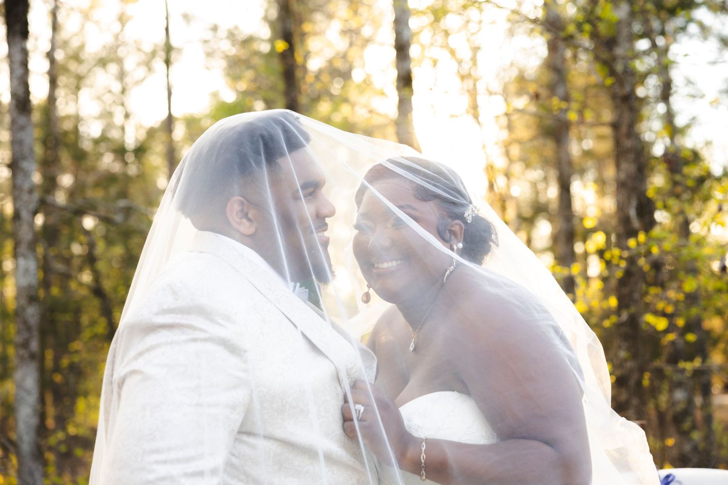 Sunlit wedding portrait through veil in front of autumn forest.
