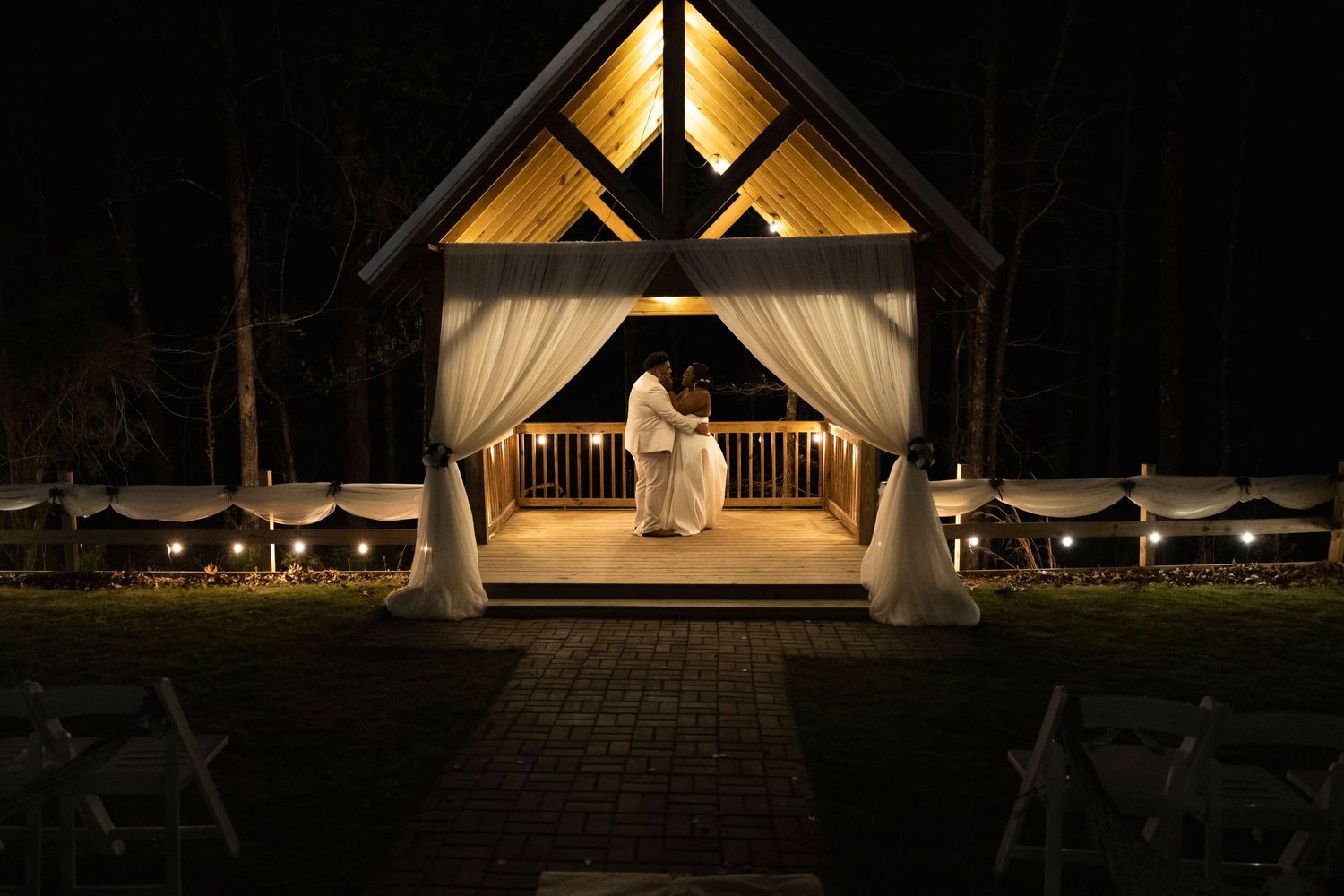 Illuminated wedding chapel at night with white draping and pathway lights.