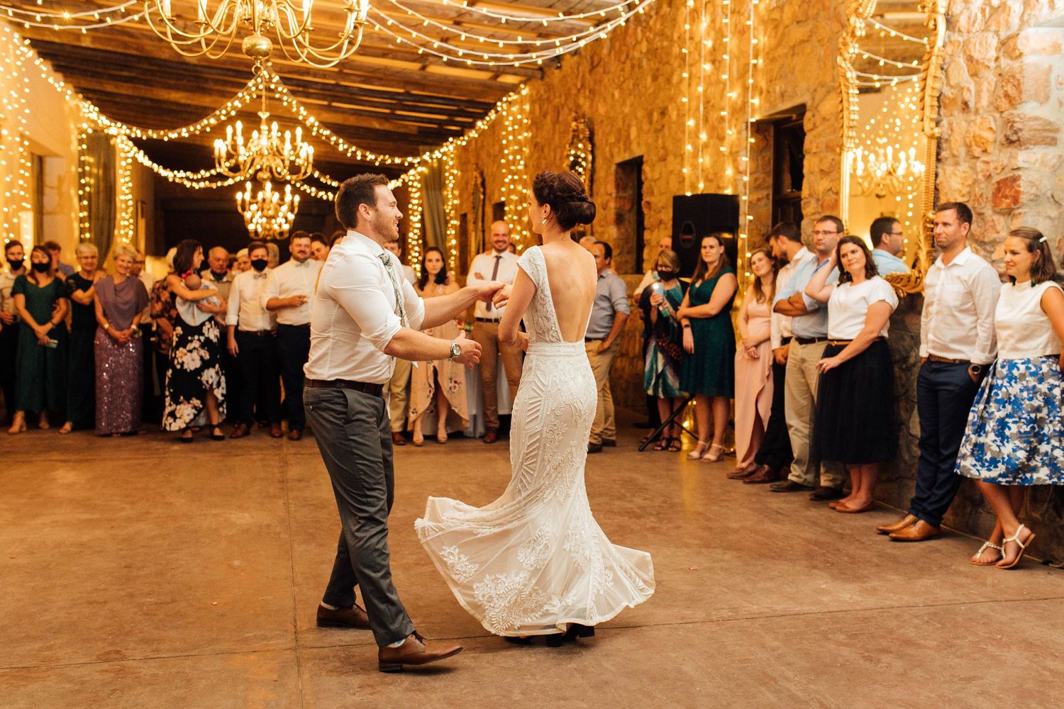 A couple dances their first dance at a wedding reception under warm string lights and chandeliers at Elandskloof.