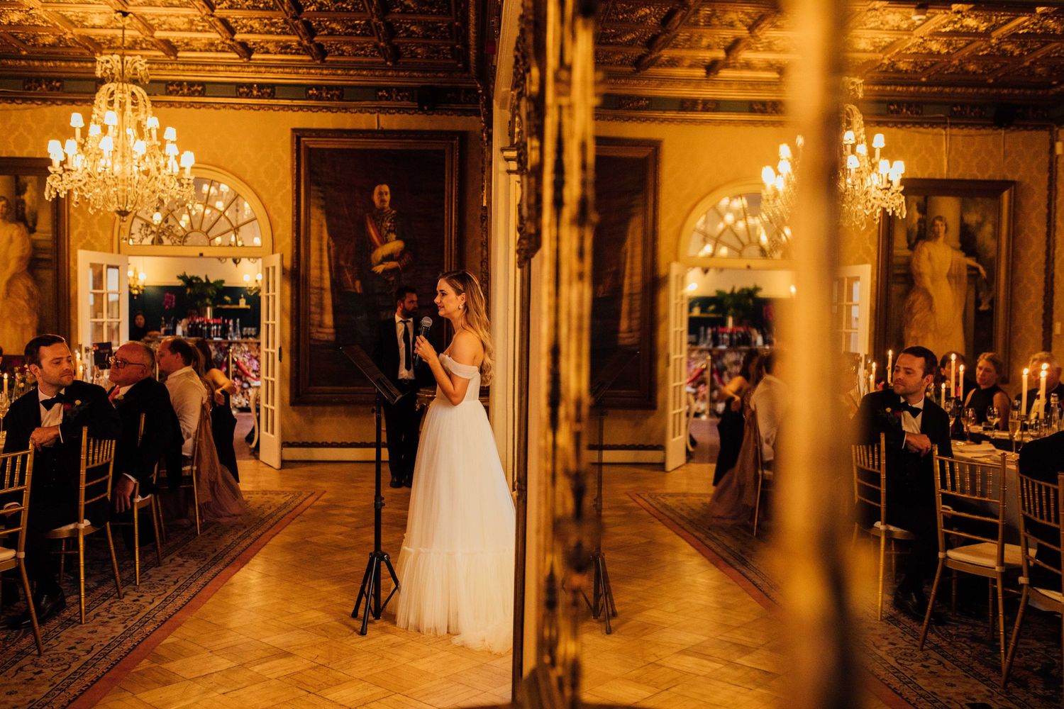 A romantic ballroom wedding scene illuminated by crystal chandeliers with a warm golden glow and vintage decor.