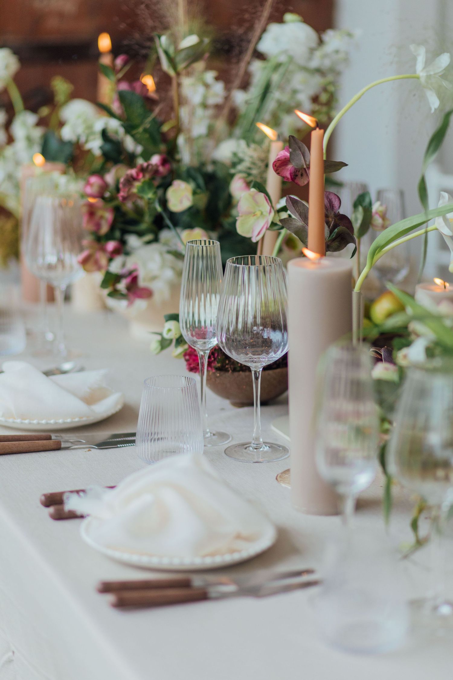Elegant wedding table setting with white linens, crystal wine glasses, and soft floral centerpieces in muted colors.