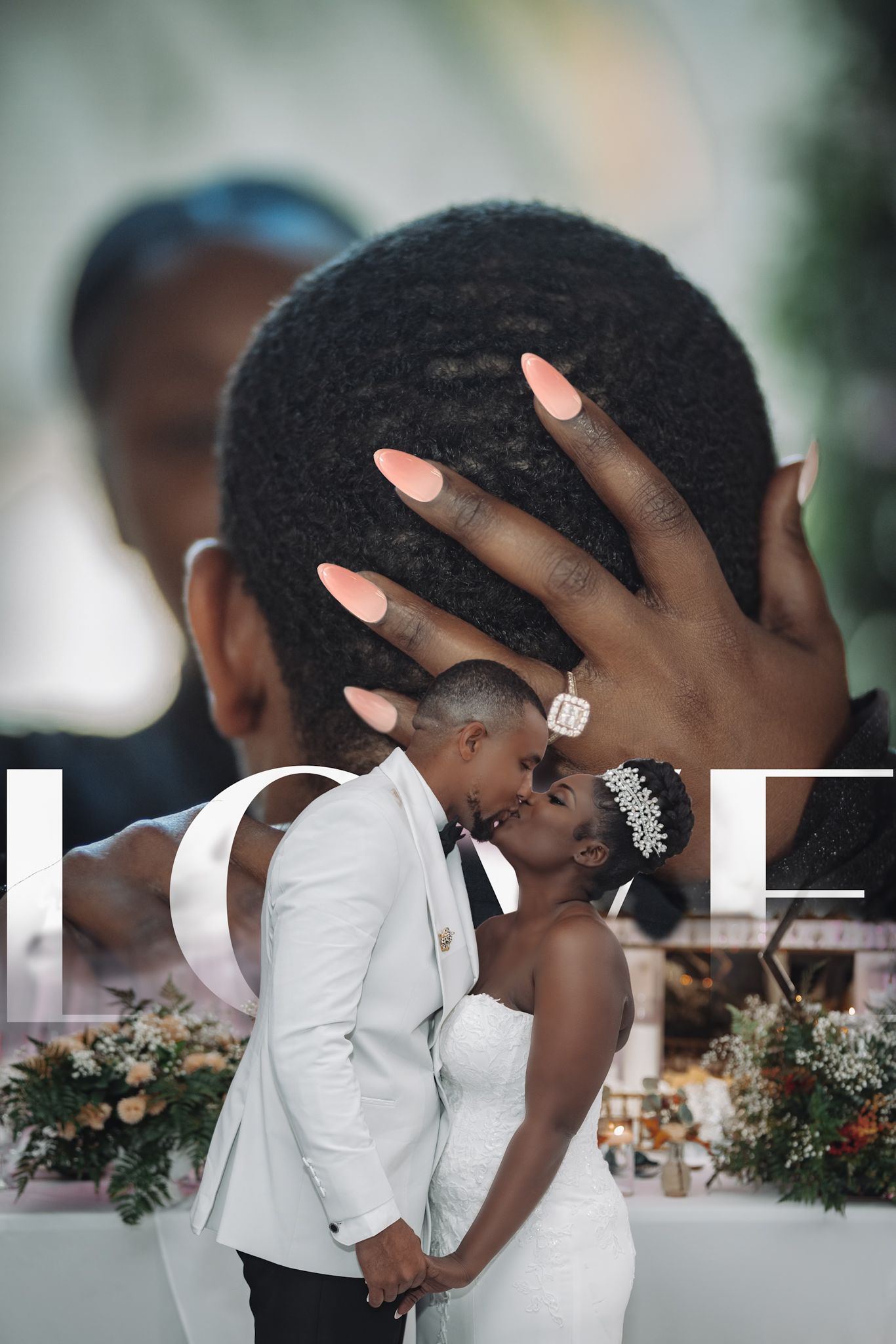 A romantic wedding couple share a tender kiss surrounded by floral decorations at their reception.