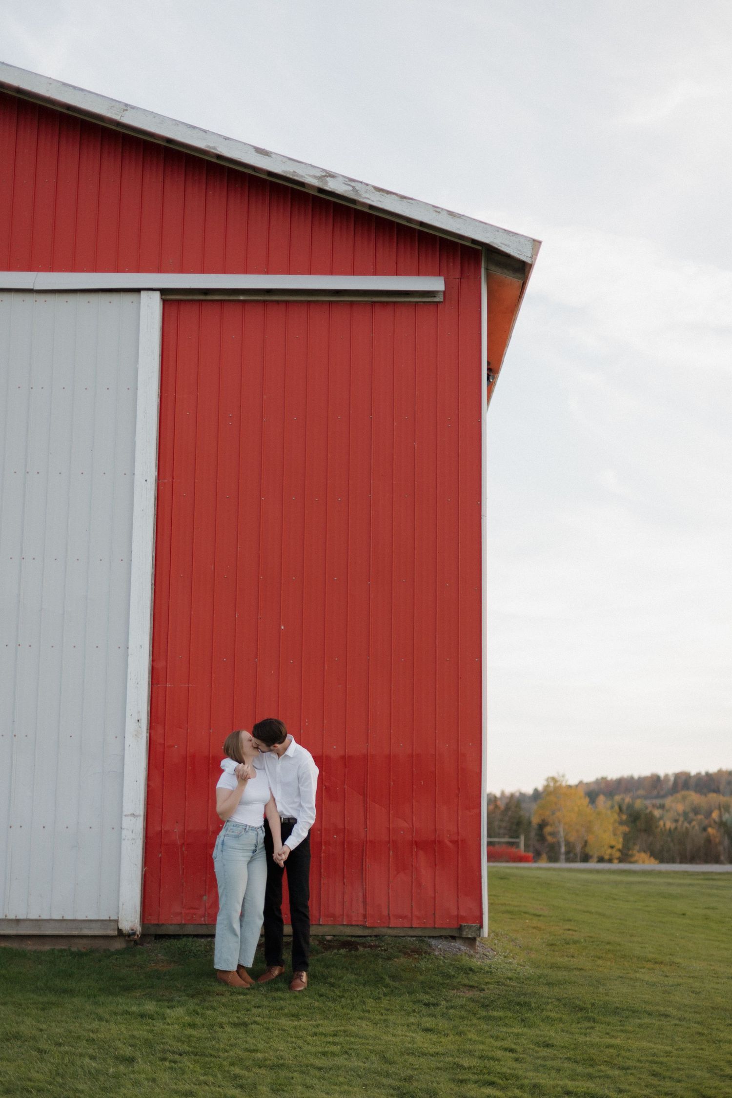 A romantic scene against a red and white barn wall set in a rural landscape on a cloudy day.