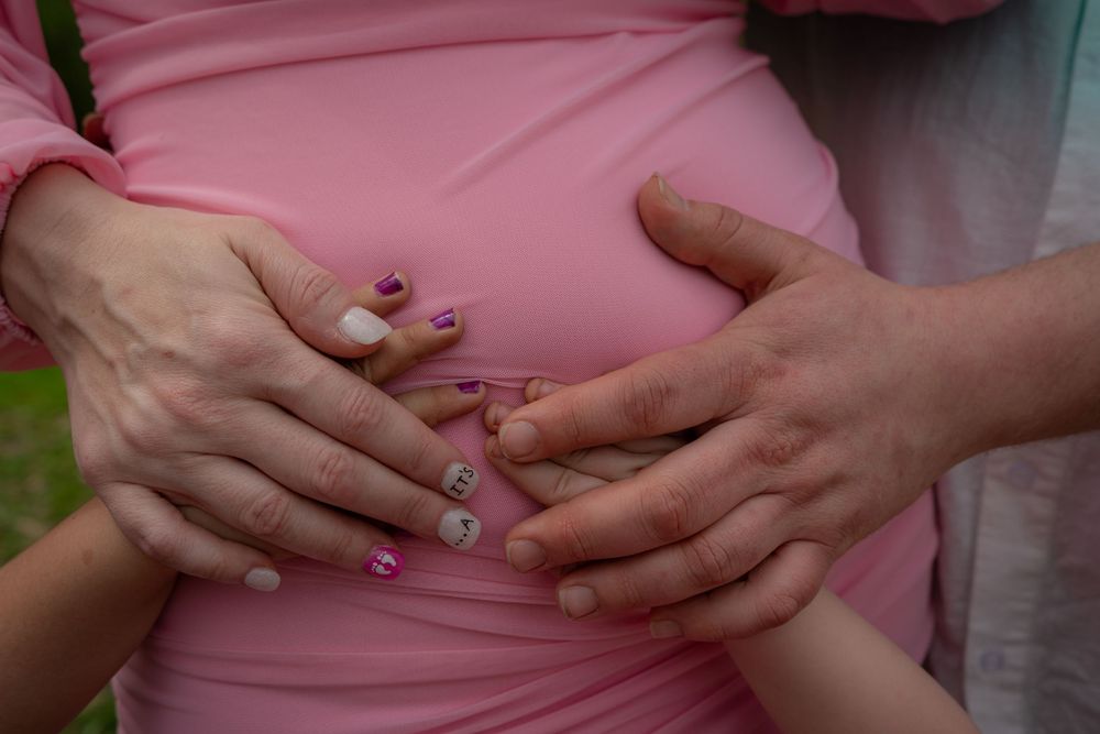 Two hands with sparkly nail polish crossed over a pink shirt in a loving heart gesture.