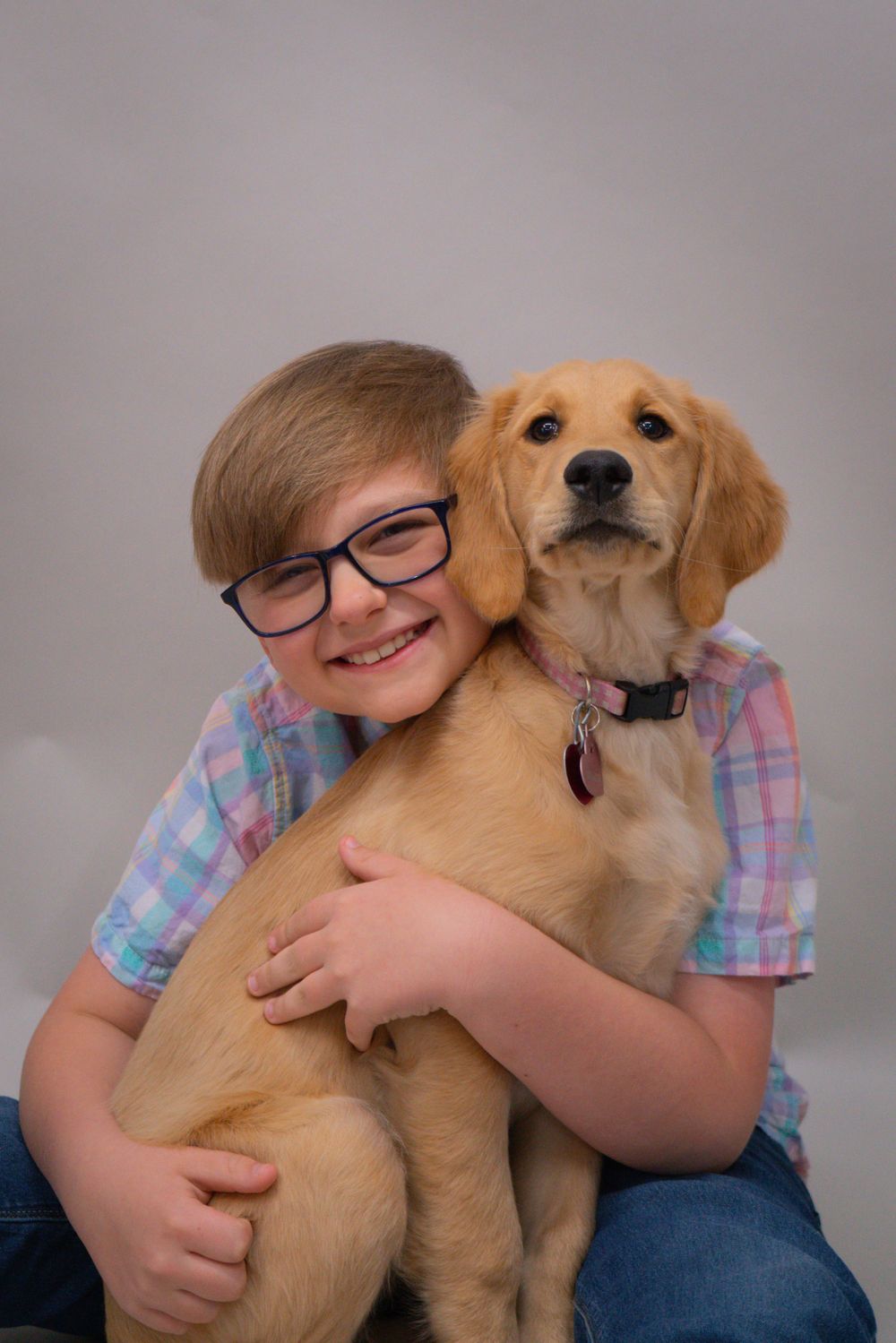 Young person in plaid shirt hugs golden retriever puppy in studio portrait setting.