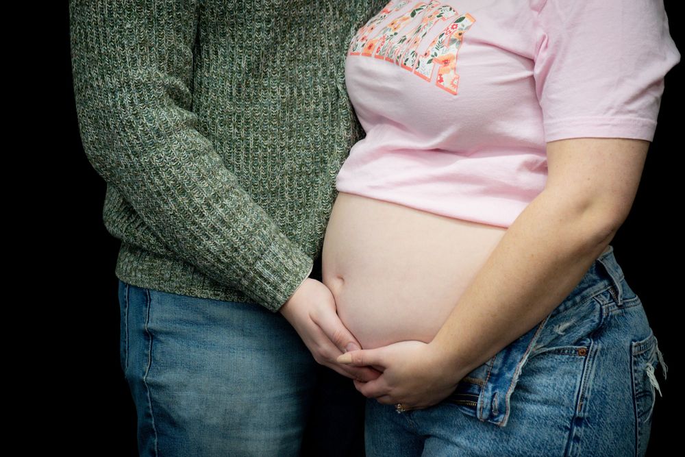 A pregnant person in jeans and pink shirt shows their growing baby bump in a series of progressive maternity photos.
