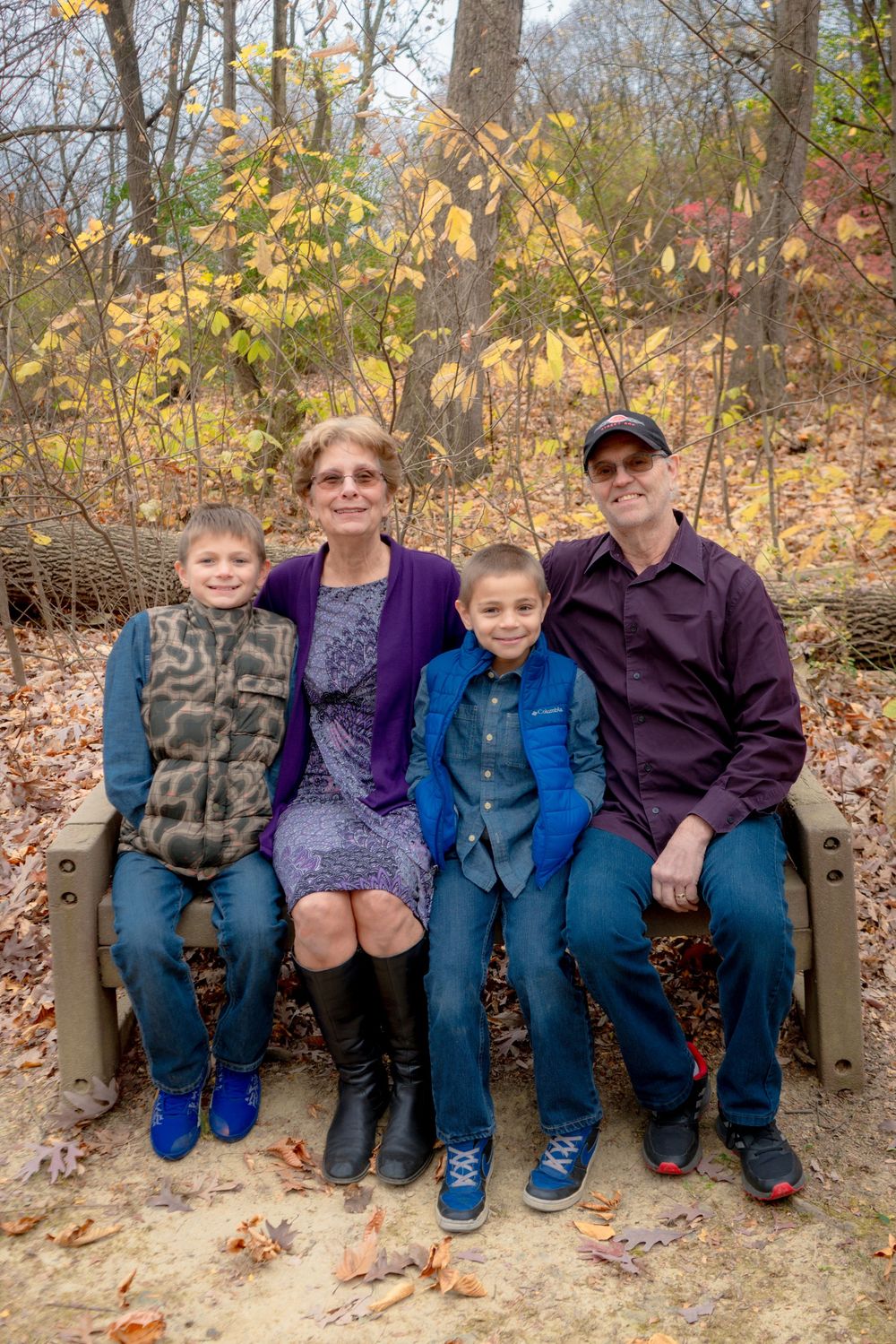 A family sits together on a wooden bench surrounded by autumn foliage in a forest setting during fall.