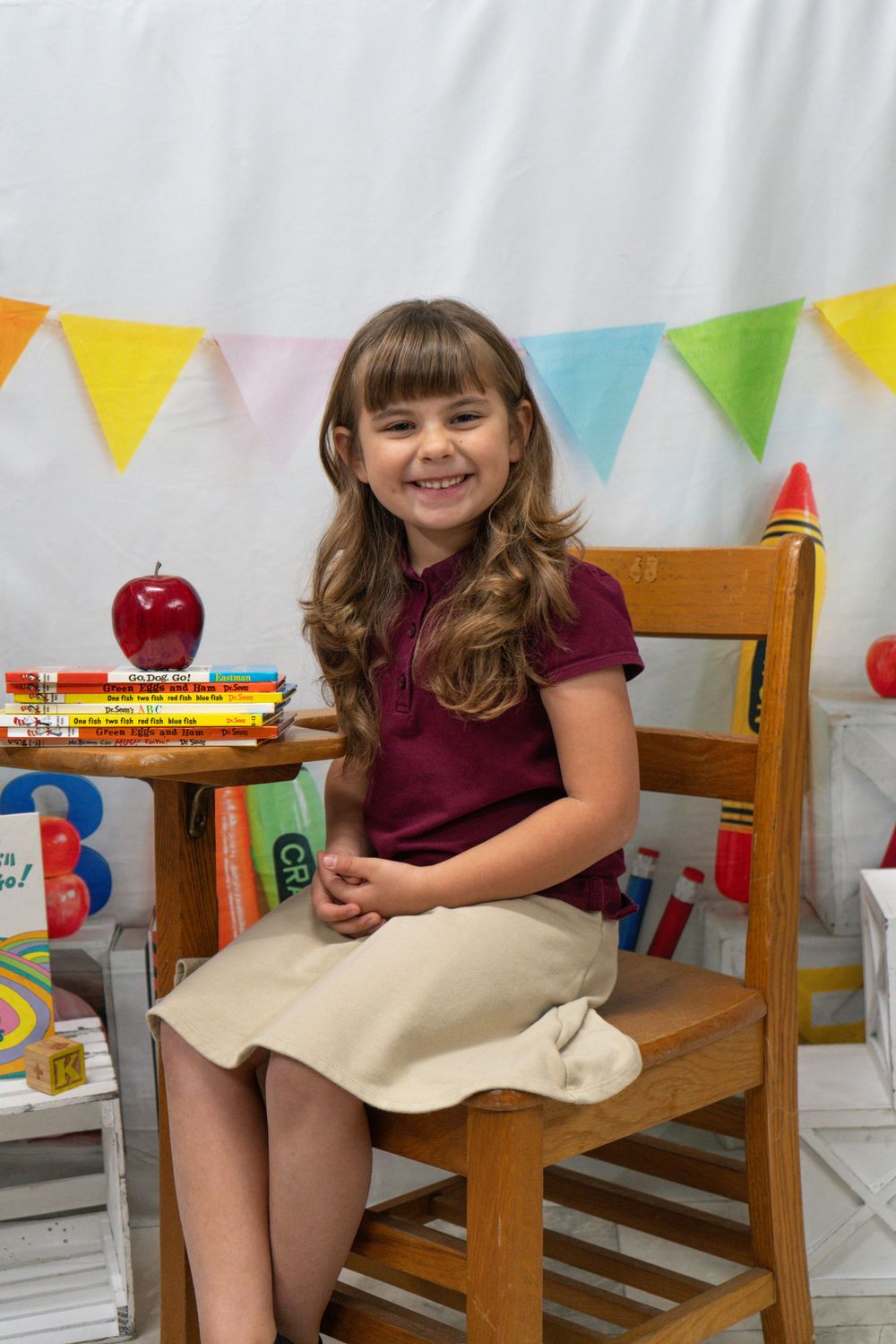 Colorful back-to-school scene with wooden chair, books, apple and festive bunting banners against white backdrop.