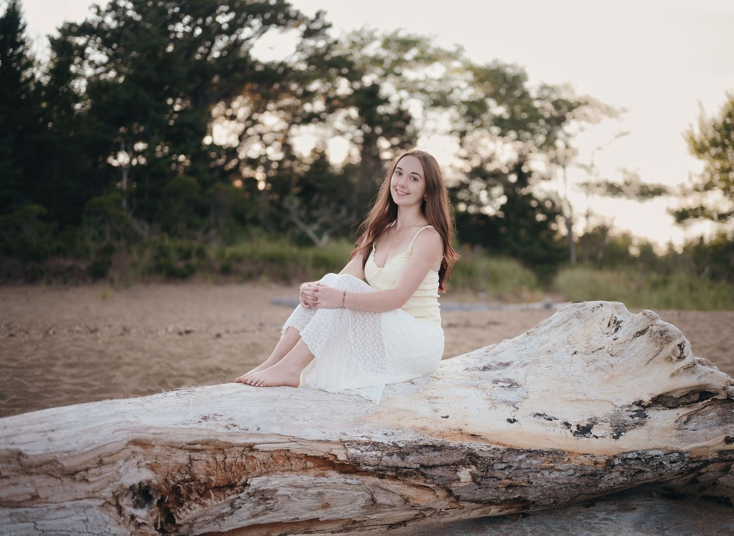 A senior in plaid sits cross-legged on a wooden dock by a serene lake surrounded by autumn trees.