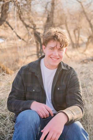 Candid outdoor portrait of someone wearing a plaid jacket sitting in tall grass.