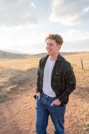 Casual portrait on a dirt path with mountains and open fields in the background.