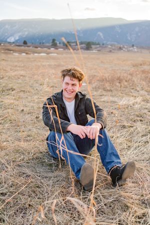 Relaxed outdoor shot of someone sitting in dry grass with mountains in the distance.