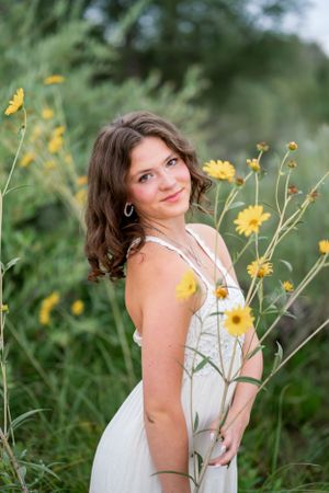 Woman in white sundress poses elegantly among blooming yellow wildflowers in natural setting.