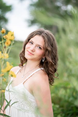 Portrait of woman in white dress standing among yellow wildflowers in soft natural light.