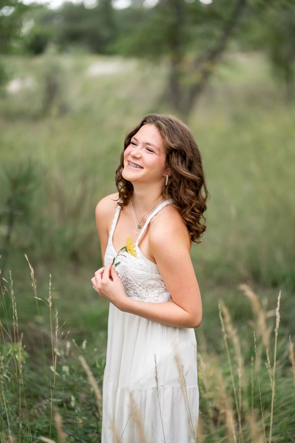 Woman in white dress smiles joyfully while standing in field of tall grass.