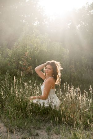 Woman in white dress poses in sunlit field during golden hour.