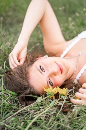 A woman with bright eyes lying in grass and wildflowers during an outdoor portrait session.