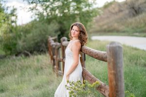 A bride in a white dress poses elegantly against a rustic wooden fence in nature.