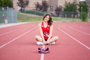 An athlete in red track uniform sits cross-legged on a running track.