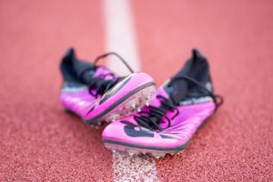 Pink and black running spikes positioned on red track surface.