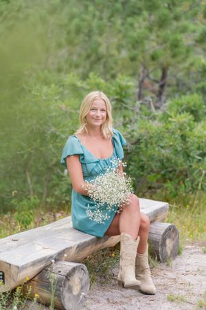 Woman in blue dress sits on rustic log bench holding baby's breath flowers.
