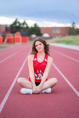 Track athlete sitting cross-legged on red running track wearing red uniform.