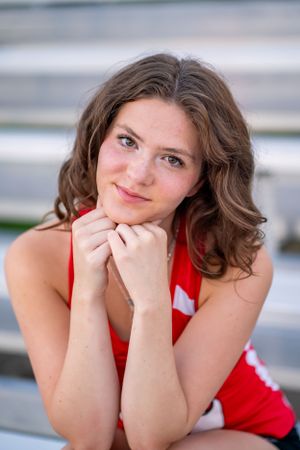 Portrait of an athlete in red uniform sitting on bleachers with hands under chin.