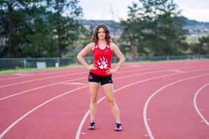 Athlete in red uniform stands confidently on curved running track.