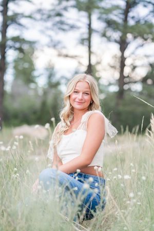 A casual summer portrait in a field of tall grass with soft natural lighting and pine trees in the background.