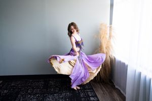 Dancer in purple costume twirls elegantly near window with flowing fabric in motion.