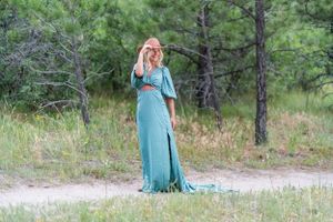 A flowing teal dress catches the light in an outdoor forest setting.