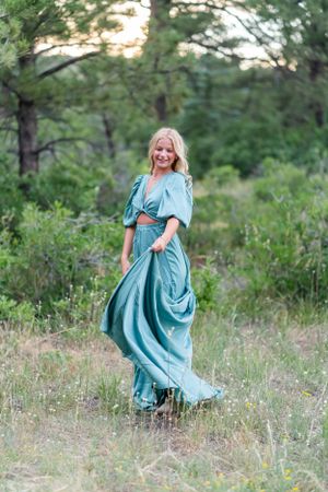 A flowing turquoise dress moves gracefully against a backdrop of pine trees at sunset.