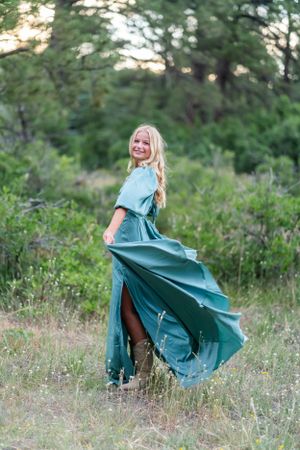 A flowing teal dress twirls dramatically in a forest clearing at sunset.